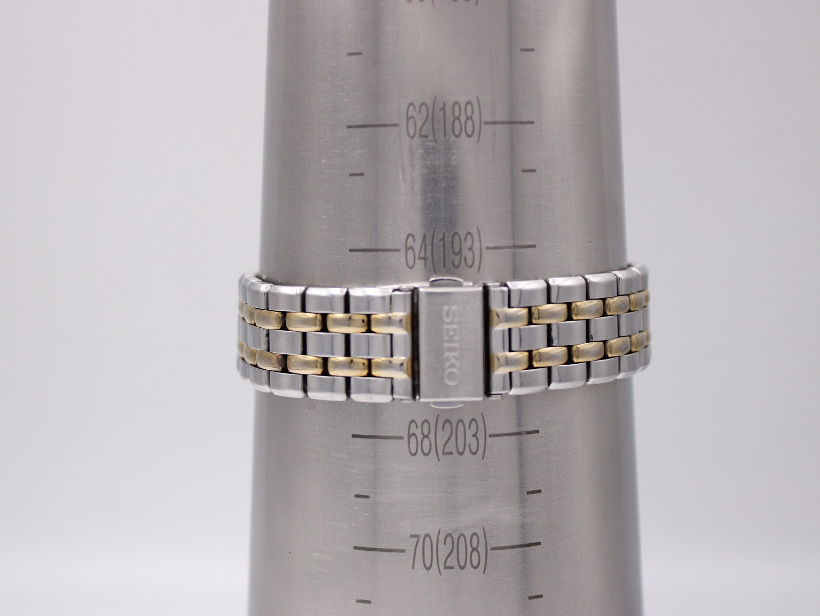 Close-up of the two-tone stainless steel bracelet with signed Seiko deployant clasp on a wrist sizing cone, indicating approximate wrist circumference.