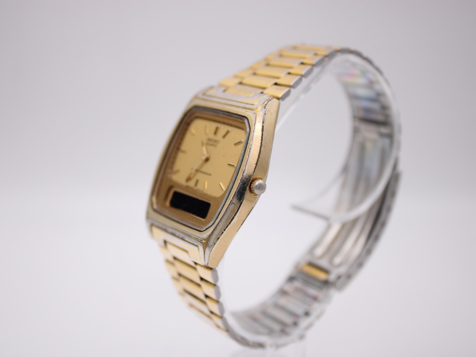Angled side view of the SEIKO H448-5000 watch, showing the gold-plated case and bracelet on a stand.
