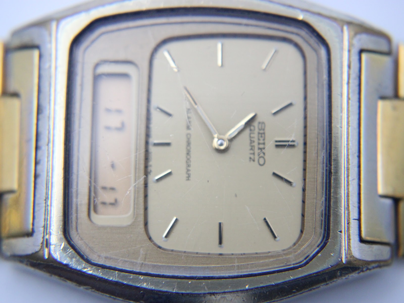 Extreme close-up of the champagne dial and digital display, revealing some scratches on the crystal surface.