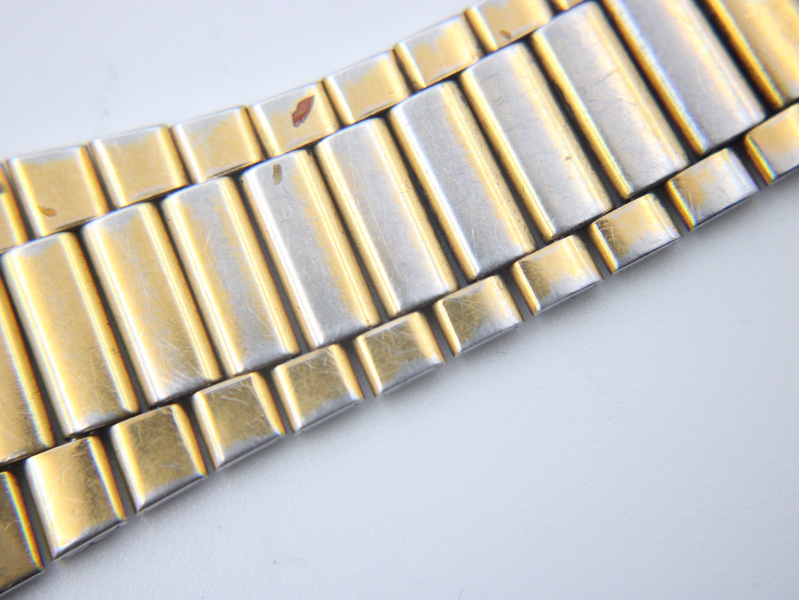 Close-up detail of the gold-plated steel bracelet links, showing wear and areas where the silver-tone base metal is visible.