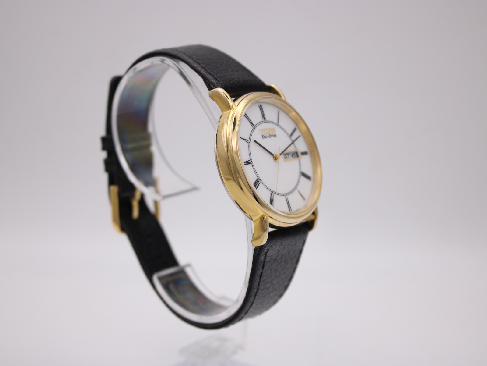 Opposite angled side view of the Citizen Eco-Drive watch on a stand, showing the black leather strap and gold buckle.