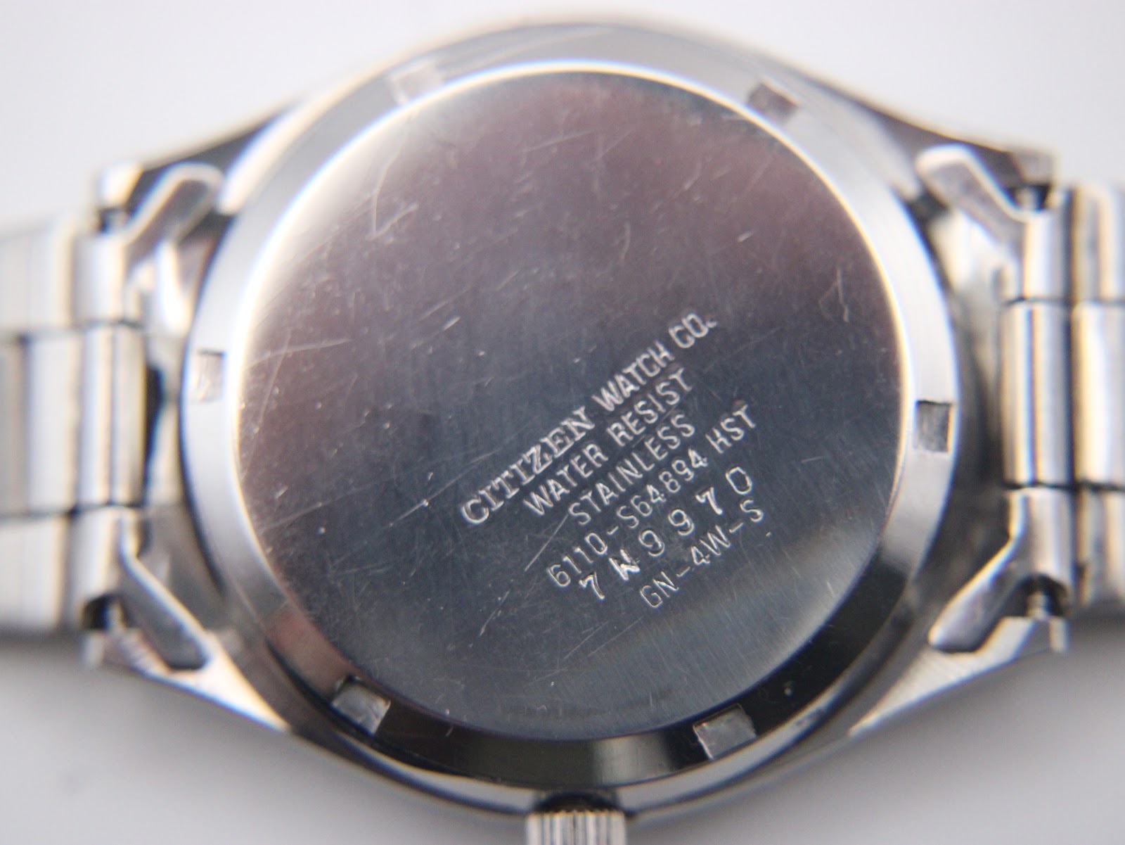 Close-up of the stainless steel case back of the Citizen watch, displaying "CITIZEN WATCH CO. WATER RESIST STAINLESS 6110-S64894 HST 7W9970 GN-4W-S" engravings.