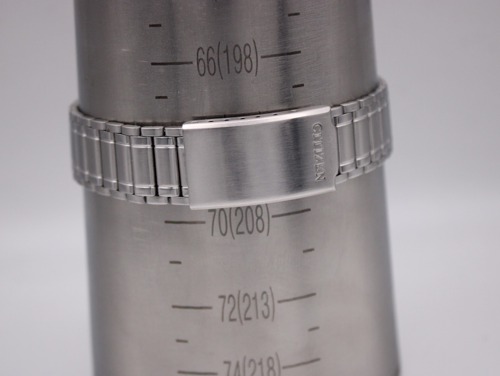 Close-up of the Citizen stainless steel bracelet's signed clasp on a wrist sizing gauge.