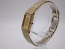 Angled side view of the Citizen watch, showing the textured gold-tone bracelet and crown, on a clear stand.