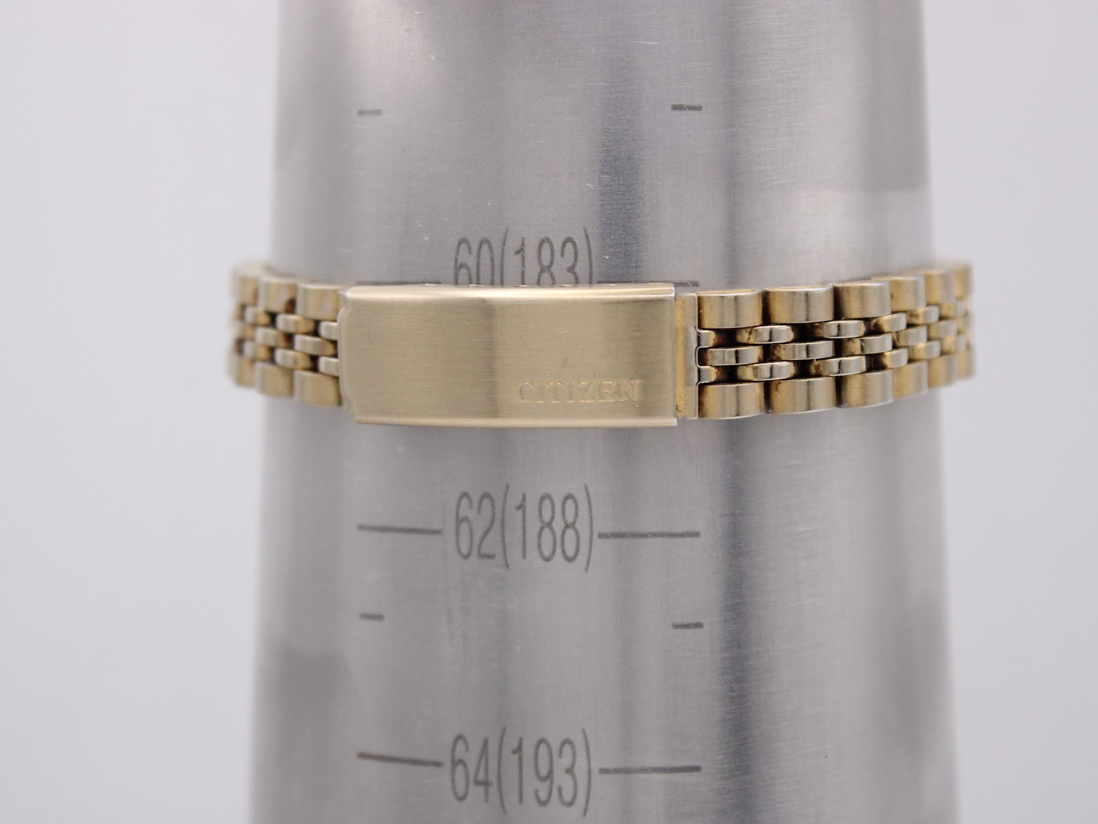 Close-up of the gold-tone Citizen steel bracelet on a wrist sizing gauge, showing the signed fold-over clasp and an approximate wrist circumference of 183mm.