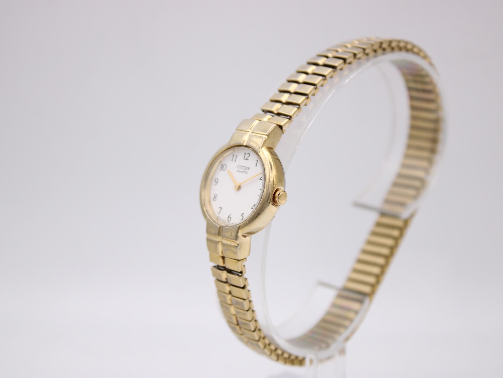 Angled right-side view of the gold tone Citizen watch showing the round case, crown, and expansion bracelet on a display stand.