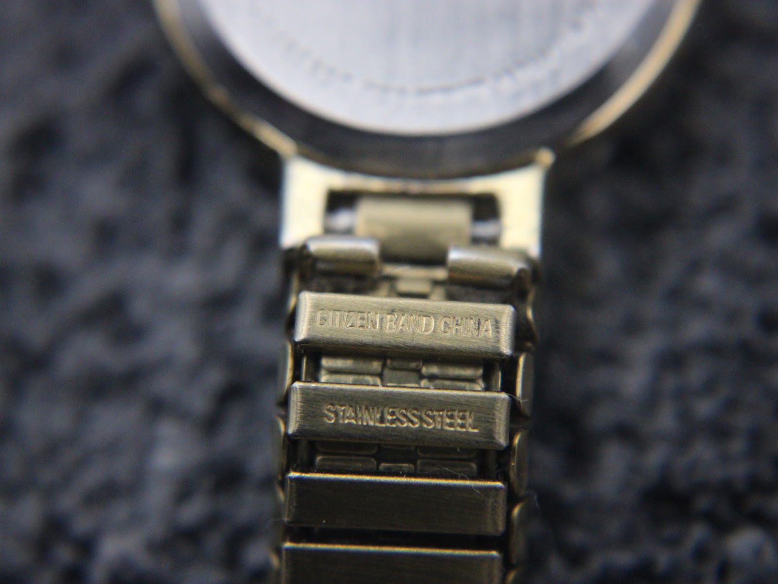 Macro shot of the underside of the gold tone expansion bracelet links, clearly showing 'CITIZEN BAND CHINA' and 'STAINLESS STEEL' engravings.