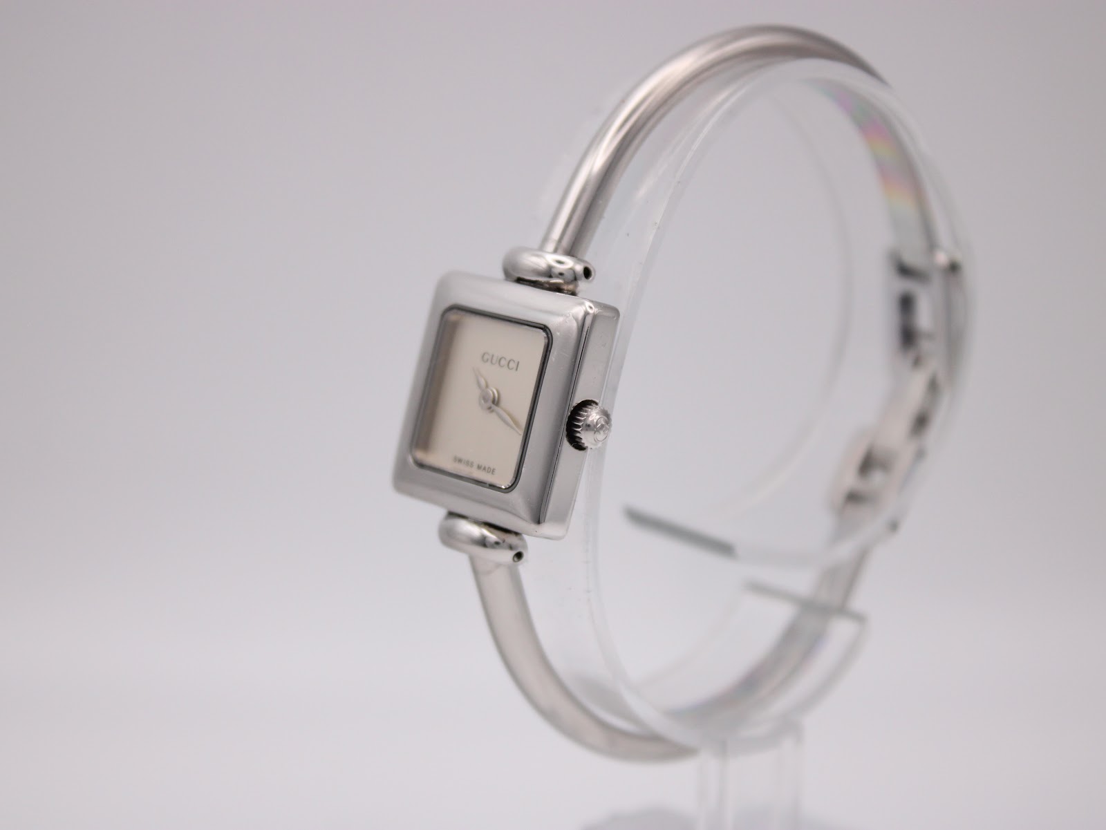 Angled view of the Gucci 1900 L watch, showing the square silver case, dial, and side profile of the bangle bracelet.