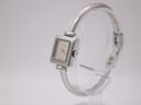 Angled view of the Gucci 1900 L watch, showing the square silver case, dial, and side profile of the bangle bracelet.