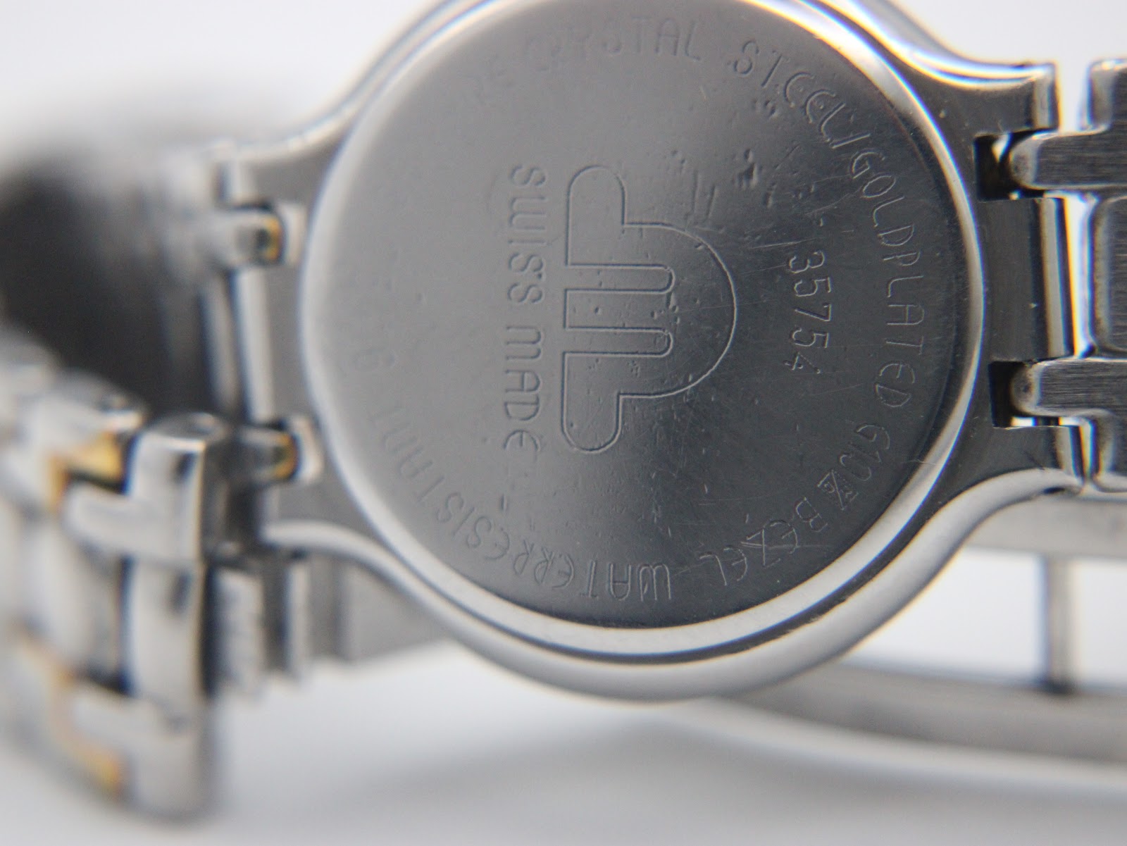 Close-up of the watch case back, showing 'SAPPHIRE CRYSTAL', 'ST.STEEL/GOLD PLATED', serial 35754, 'WATER RESISTANT', and 'swiss made' engravings.