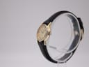 Side-angle view of the Tissot watch on a stand, highlighting the gold-tone case and crown from the right.
