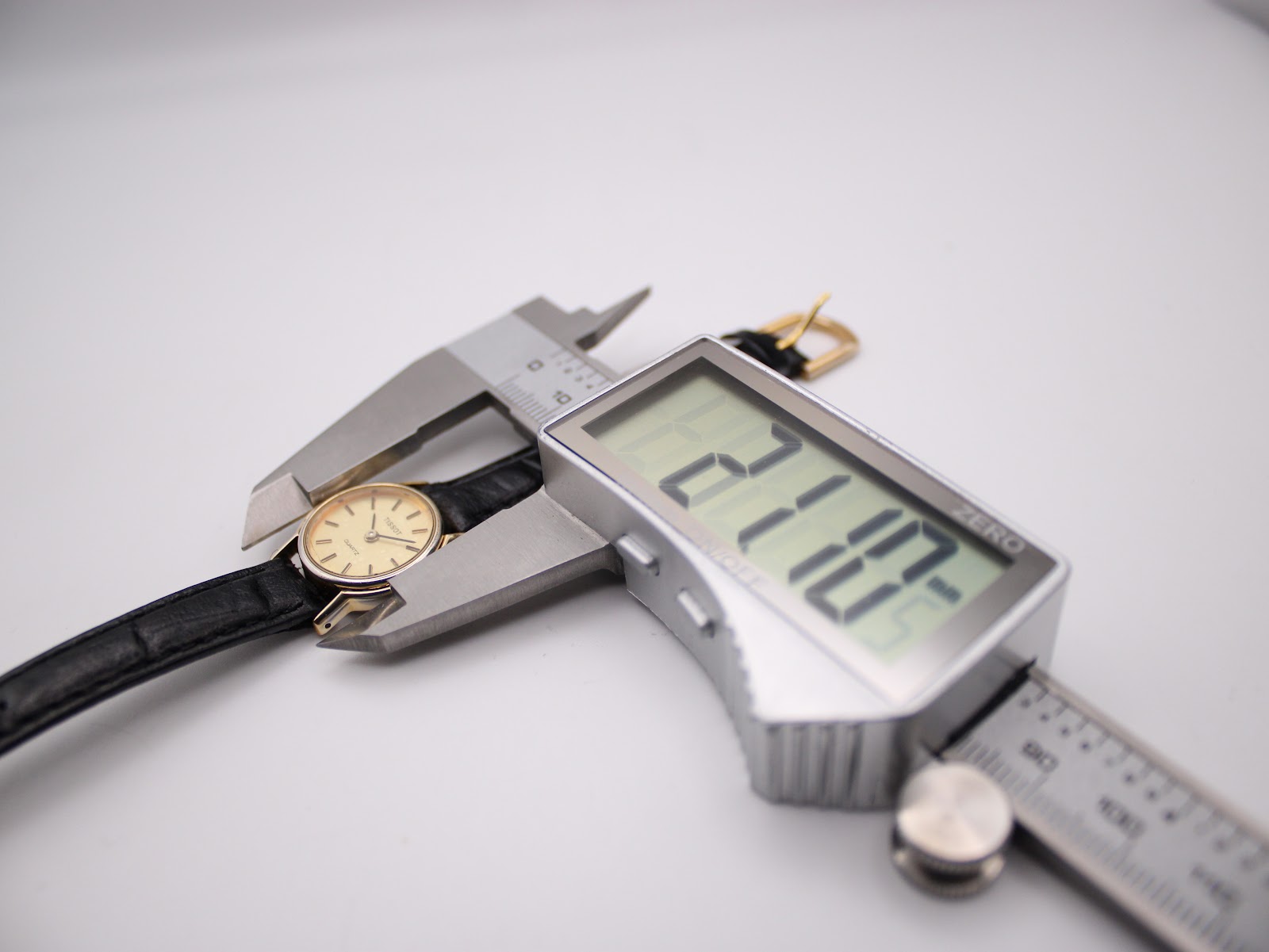 Close-up of a digital caliper measuring the Tissot watch case diameter at 21.10mm, with the strap visible.