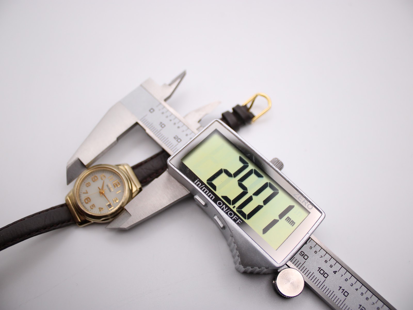 Digital caliper measuring the case diameter of the Citizen Eco-Drive watch, showing a precise measurement of 28.01mm.
