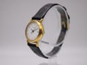 Angled right-side view of the Tissot C 212 watch on a display stand, highlighting the gold-tone case, crown, and black strap.