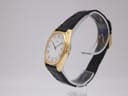 Angled side view of the gold-plated Seiko watch, showing the crown and the profile of the tonneau case and black leather strap.