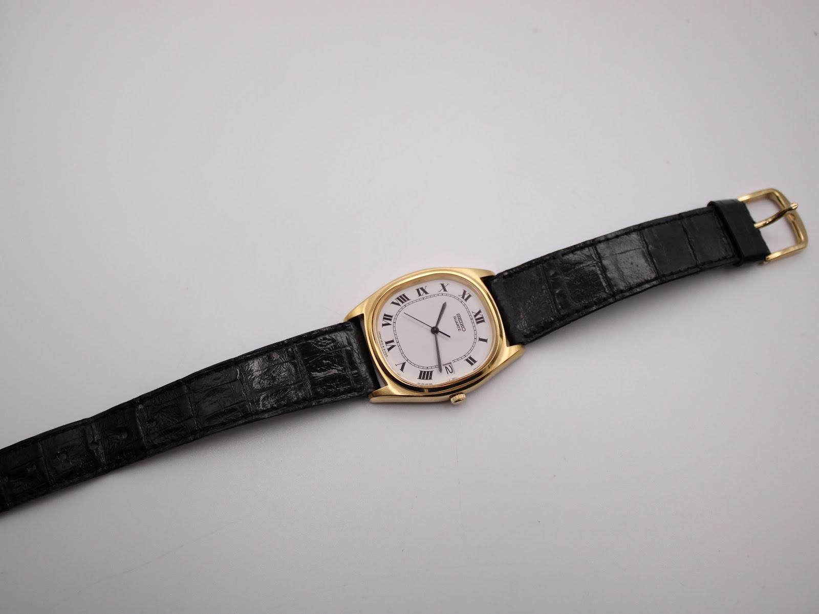Overhead view of the Seiko watch laid flat, displaying the full black leather strap with its gold-tone buckle.
