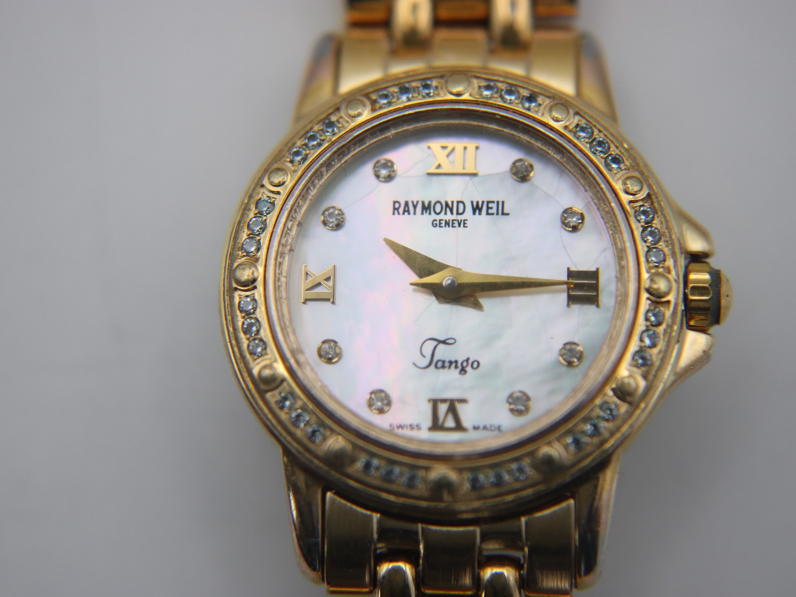 Detailed close-up of the Raymond Weil Tango mother of pearl dial, with gold Roman numerals, crystal hour markers, gold hands, and the 'Tango' script.