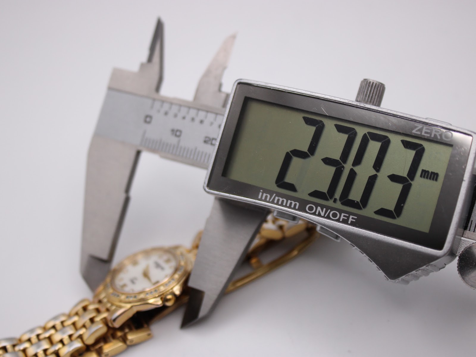 Digital caliper display showing a precise measurement of 23.03mm across the watch case, with the watch visible in the background.
