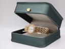 The Raymond Weil Tango watch resting inside a dark green presentation box with a gold crown emblem on the lid.