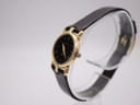 Angled view of the gold-tone Gucci 3400 L watch on a clear display stand, showing the case and black strap.