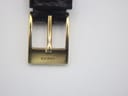 Close-up of the gold-tone buckle on the black leather strap, with "GUCCI" engraved.