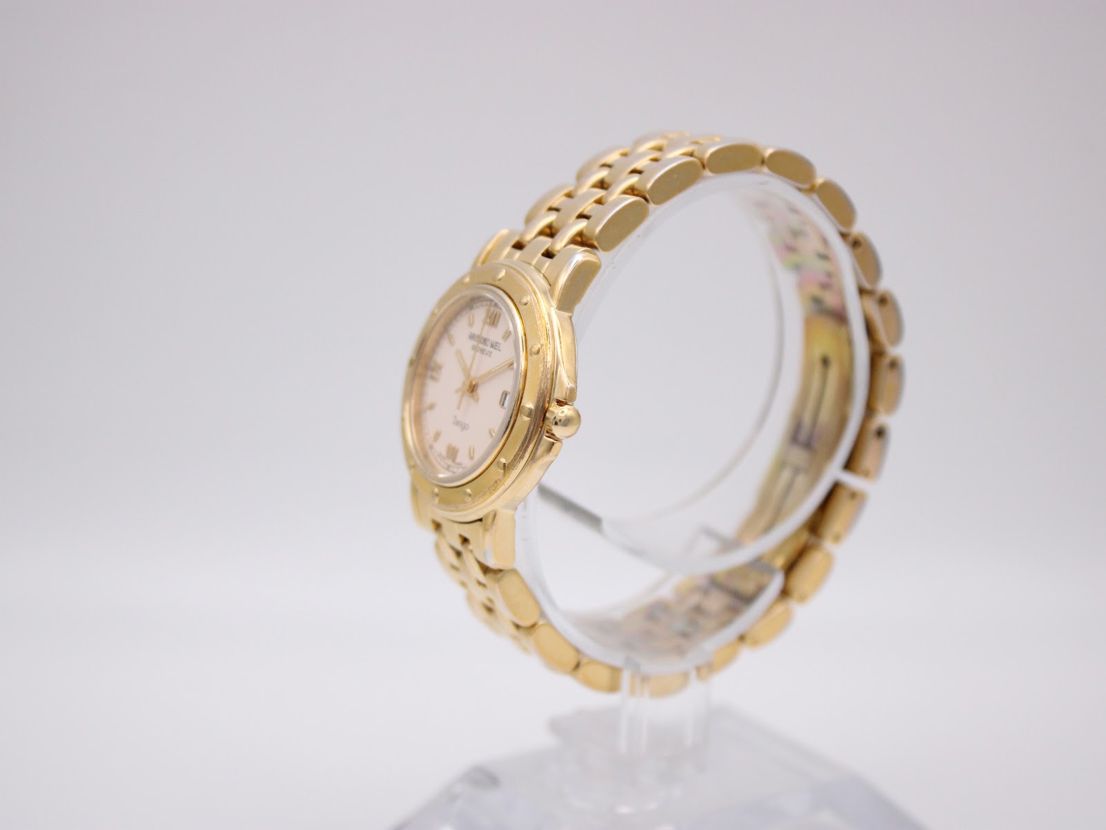 Angled side view of the Raymond Weil Tango watch on a display stand, showing the gold case and two-tone bracelet.