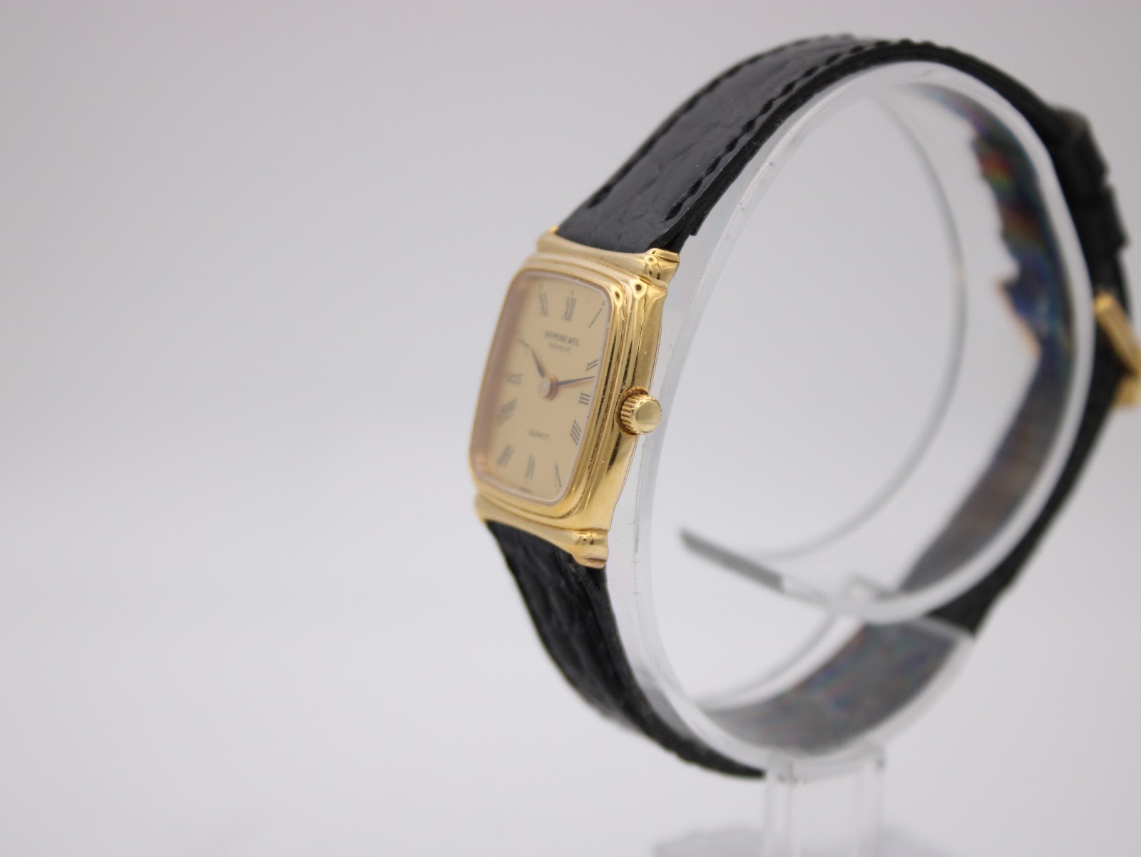 Angled side view of the Raymond Weil 5744 watch, highlighting the gold case and crown on a white display stand.