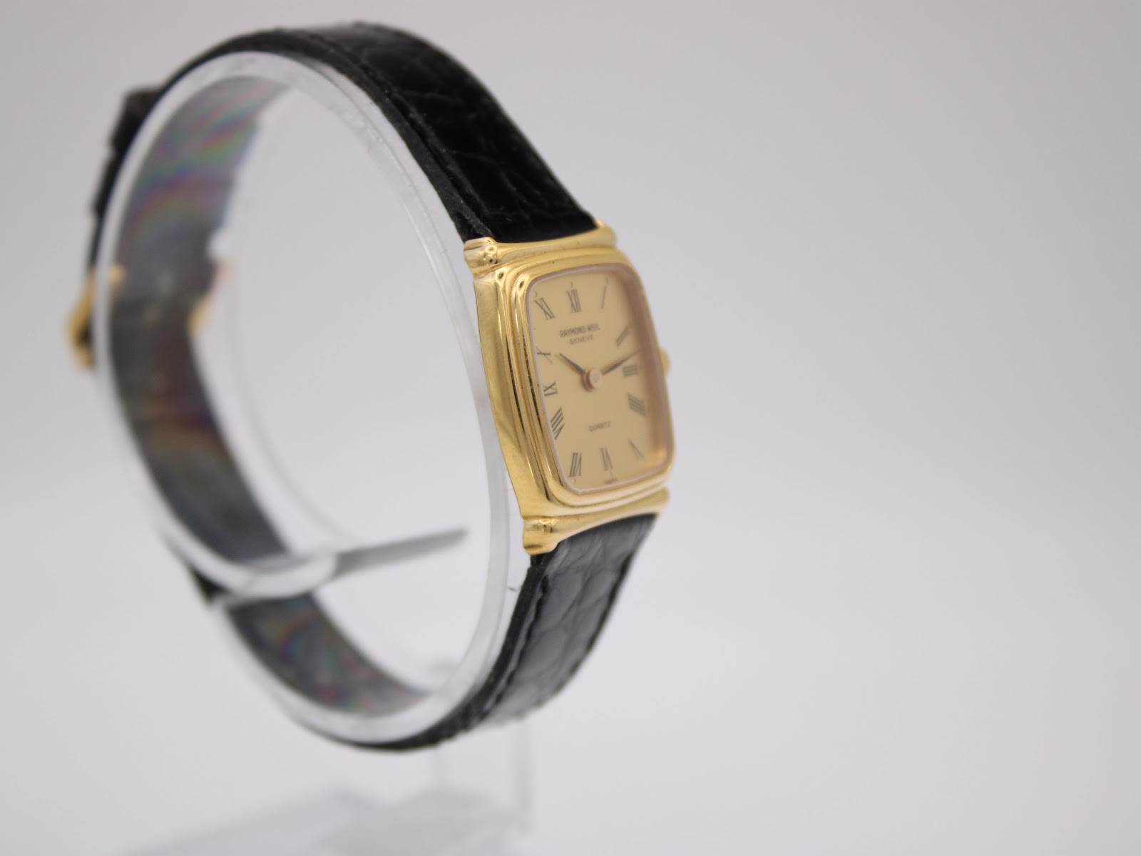 Another angled side view of the Raymond Weil 5744 watch, showcasing the profile of the rectangular gold case and black leather strap.