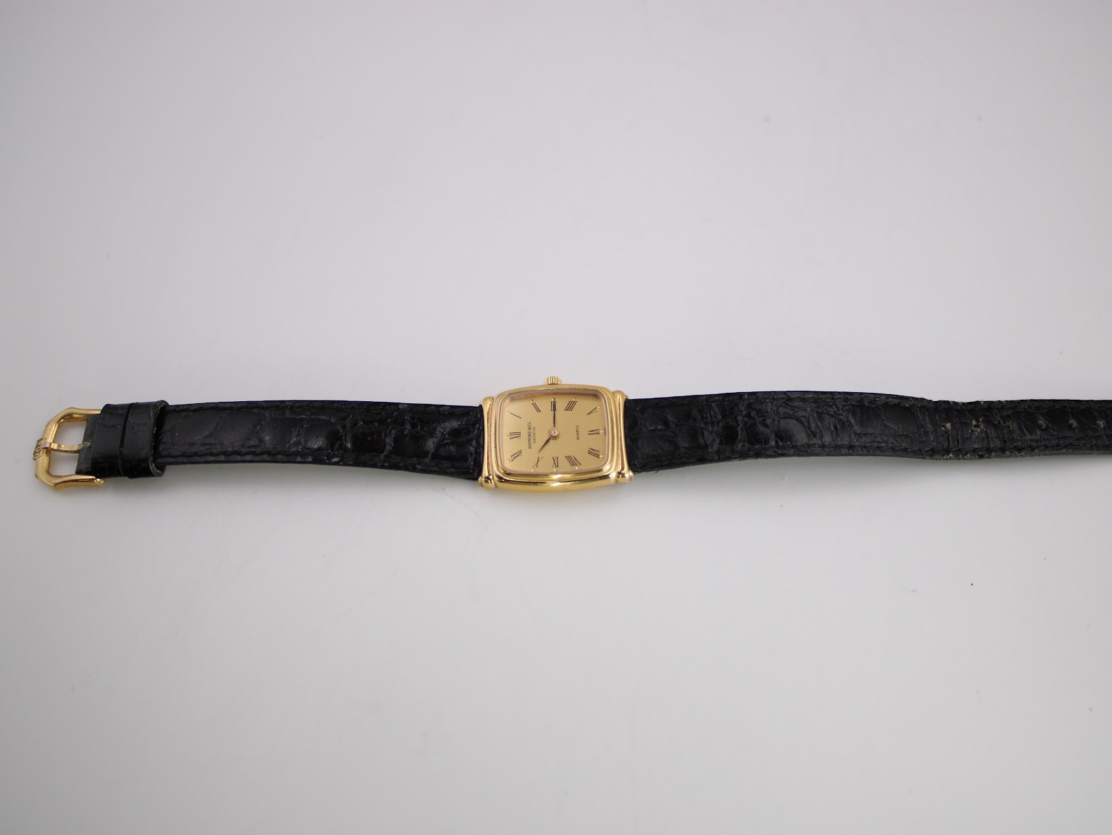 Full flat lay view of the Raymond Weil 5744 watch, showing the entire length of the black leather strap and the gold rectangular case.