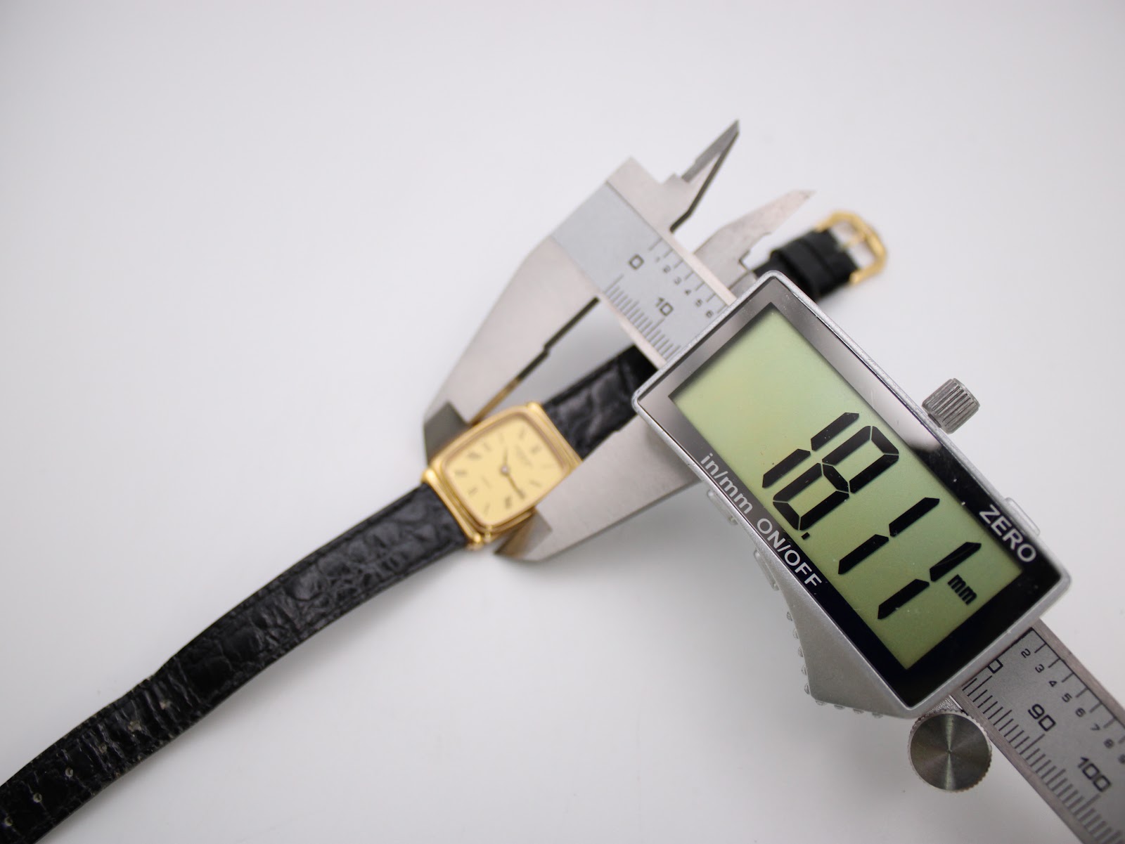 A digital caliper measuring the case diameter of the Raymond Weil 5744 watch, displaying a precise reading of 18.1mm.