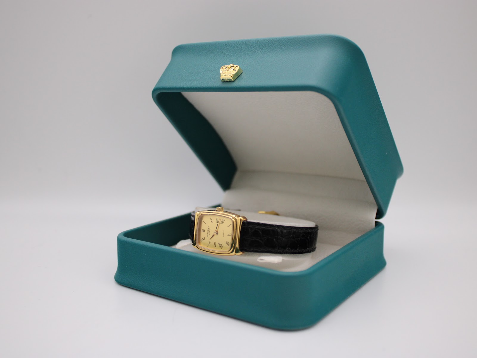 The Raymond Weil 5744 watch sitting inside a teal coloured generic display box with a cream interior.