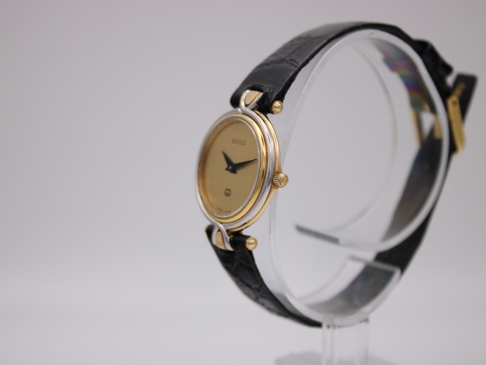 Angled right-side view of the two-tone Gucci 4500 L watch on a clear stand, showing the crown.