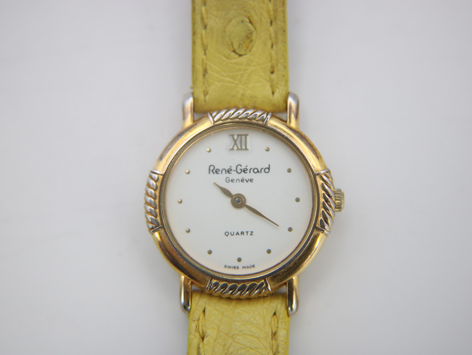 Direct front view close-up of the René Gérard Geneve watch dial, with Roman numeral XII, dot indices, and gold-toned hands.