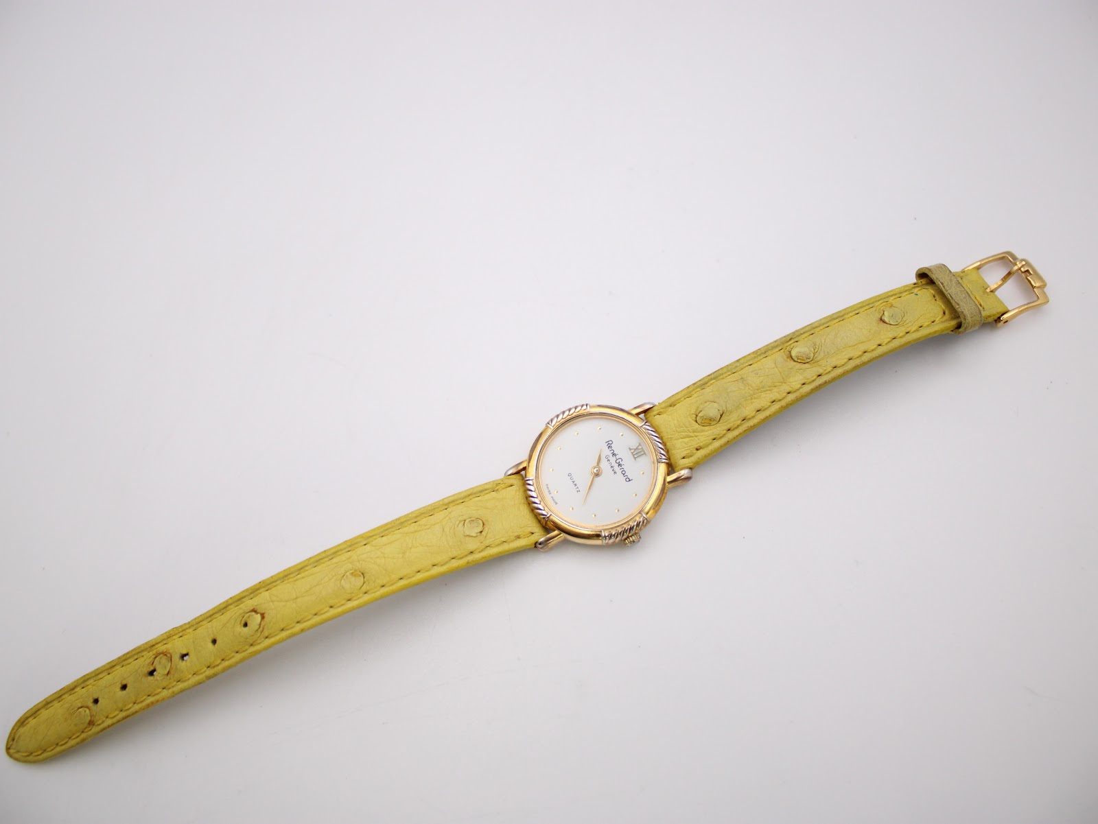 Full length view of the René Gérard watch on its yellow textured leather strap, laid flat with the buckle visible.