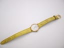 Full length view of the René Gérard watch on its yellow textured leather strap, laid flat with the buckle visible.