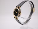 Angled side view of the Gucci 2000L watch on a clear display stand, highlighting the ribbed gold-tone case and crown.