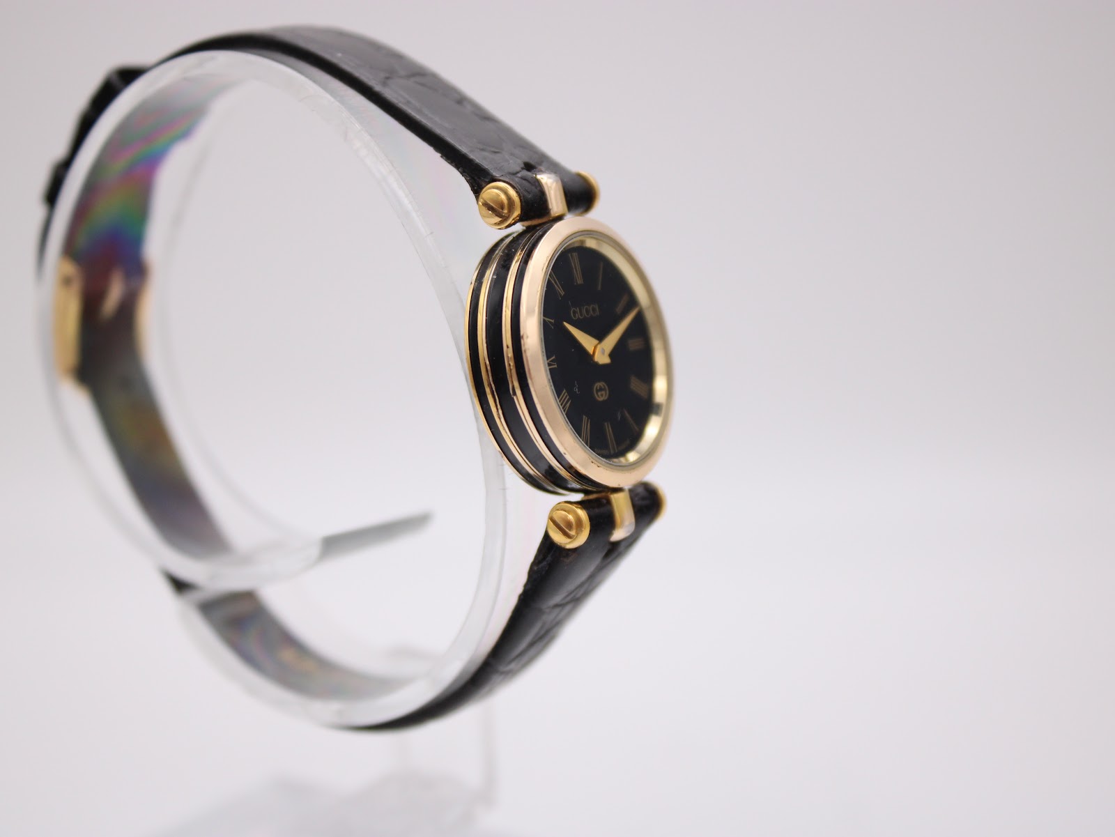 Another angled side view of the Gucci 2000L watch on a display stand, showing the elegant profile of the gold-tone case.