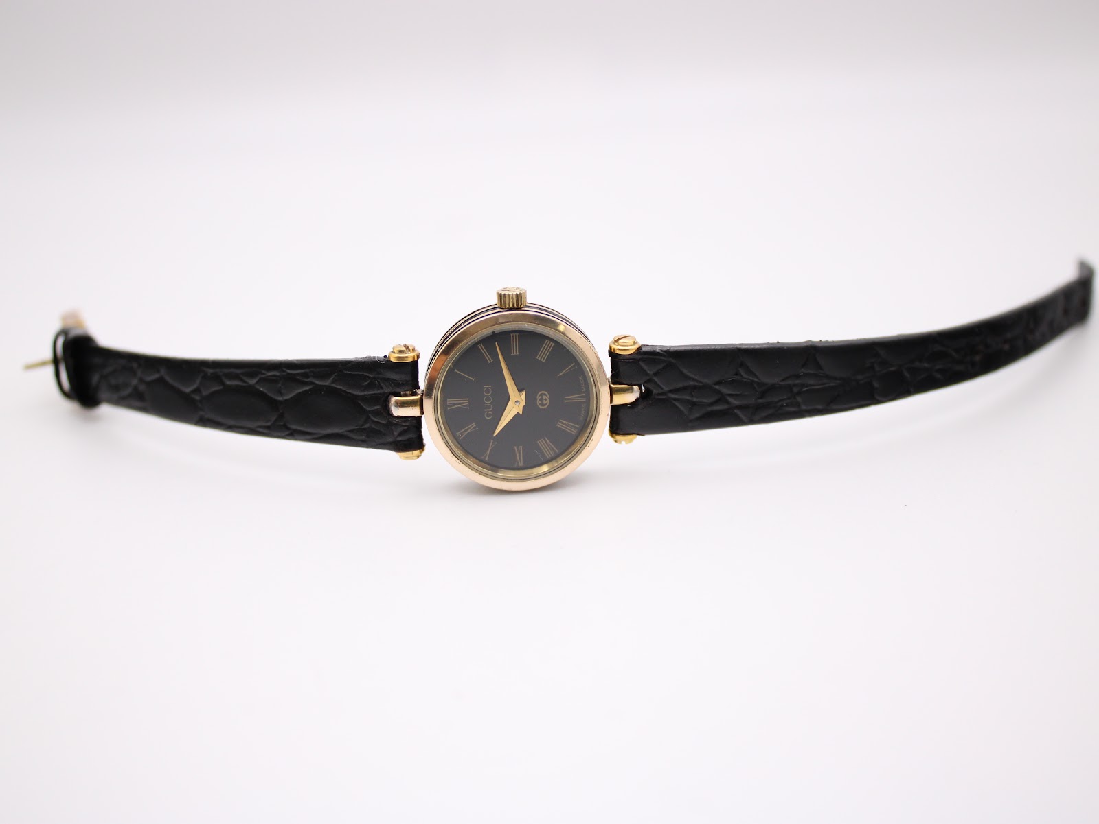 Top-down view of the Gucci 2000L watch, showing the full length of the black crocodile-effect leather strap and the gold-tone case and black dial.