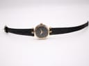 Top-down view of the Gucci 2000L watch, showing the full length of the black crocodile-effect leather strap and the gold-tone case and black dial.