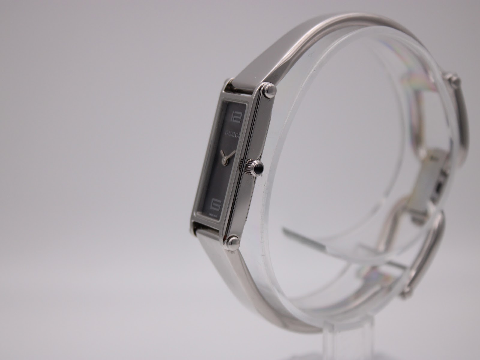 Side-angle view of the Gucci 1500 L watch, showing the crown and the curved stainless steel bangle bracelet.