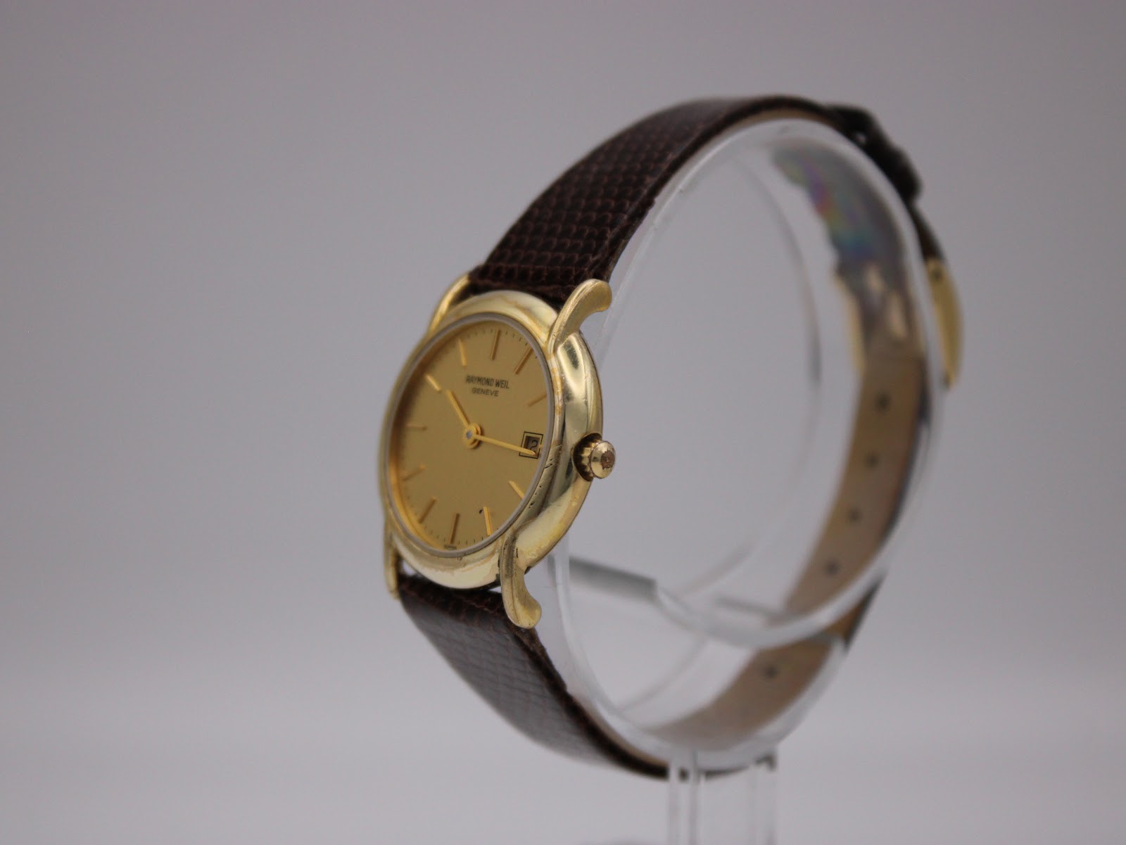 Angled side view of the Raymond Weil 9940 watch, highlighting the gold case and textured brown leather strap.