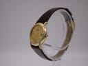 Angled side view of the Raymond Weil 9940 watch, highlighting the gold case and textured brown leather strap.