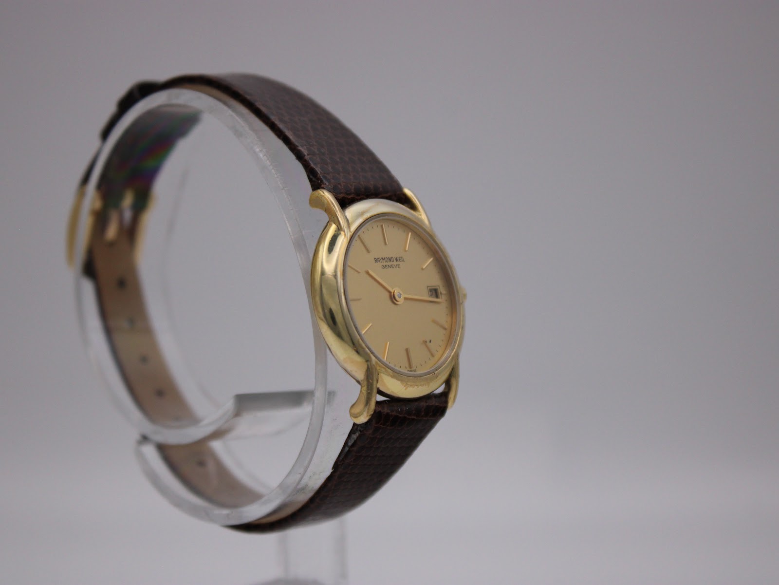 Another angled view of the watch, showing the minimalist gold dial and the curve of the case on a clear display.