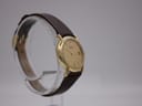 Another angled view of the watch, showing the minimalist gold dial and the curve of the case on a clear display.