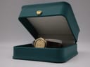 The Raymond Weil watch placed inside a generic teal display box with a gold crown emblem, suggesting presentation.