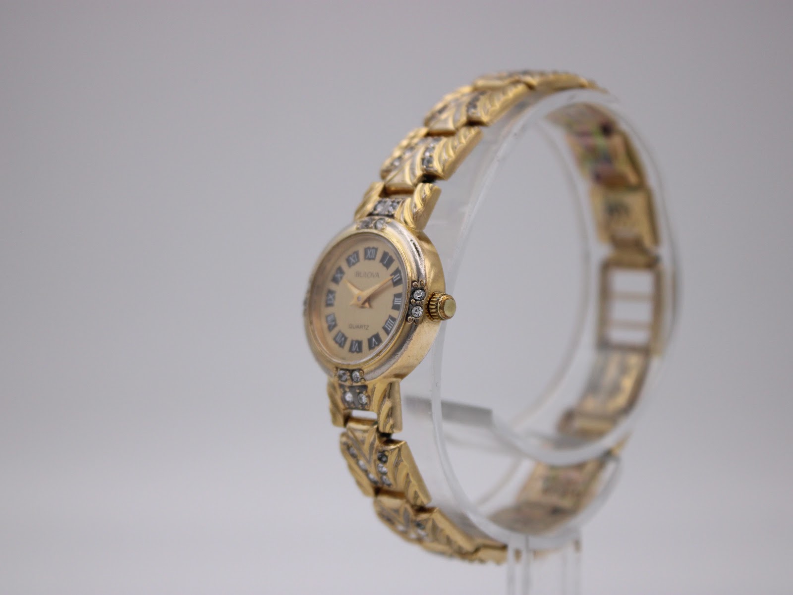 Angled view of the Bulova watch, showing the right side of the case and crown, with the gold-tone, rhinestone-set bracelet.