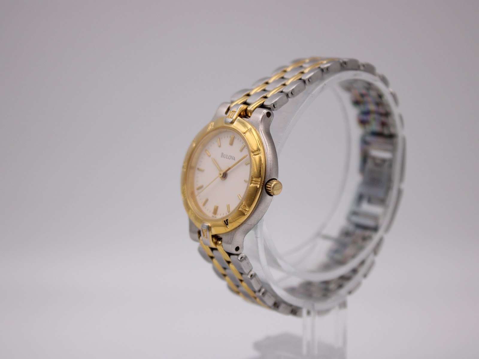 Angled view of the Bulova two-tone watch, showing the case and bracelet links on a clear stand.