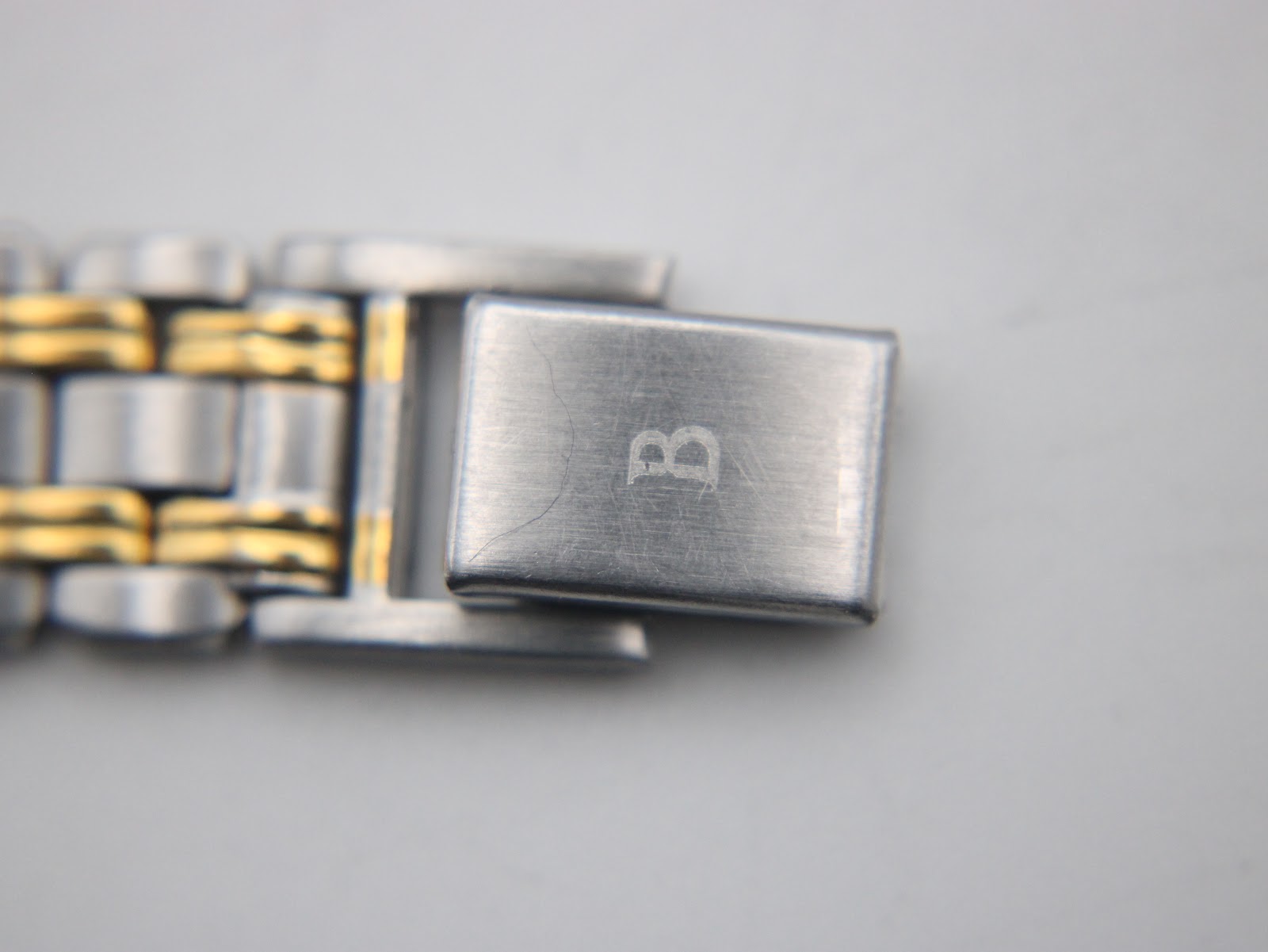 Close-up of the two-tone bracelet's fold-over clasp, showing an engraved 'B' logo.