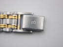 Close-up of the two-tone bracelet's fold-over clasp, showing an engraved 'B' logo.