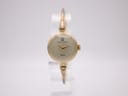 Front view of the Michel Herbelin gold-tone bangle watch with a cream dial on a clear stand.